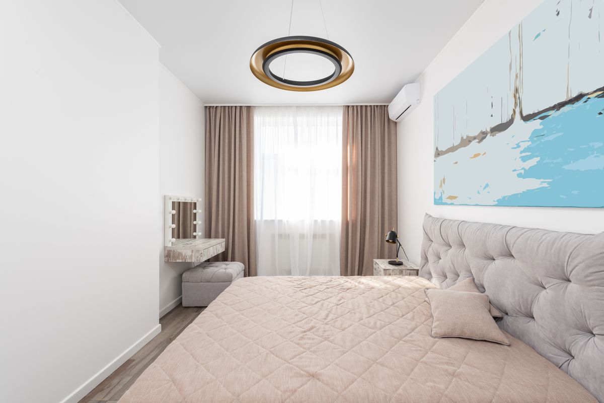 A neatly made bed in a light bedroom with curtains and a window.