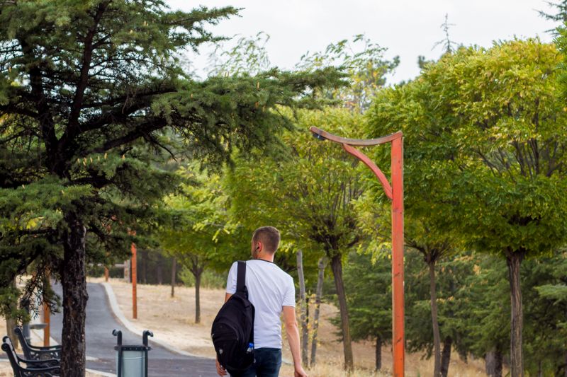 Man carrying a backpack while walking along a tree-lined park path.