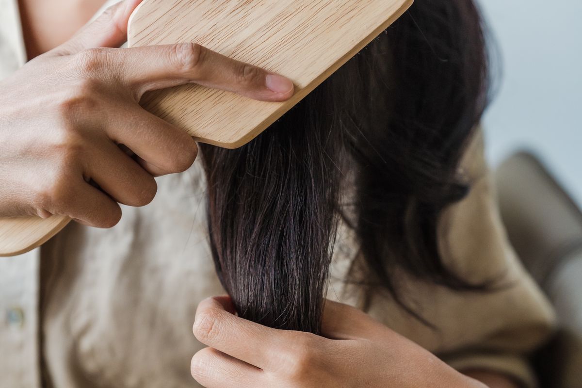 Close-up of hands gently brushing long dark hair with a wooden brush.