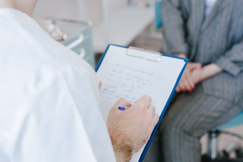 Healthcare professional taking notes on a clipboard during a conversation.