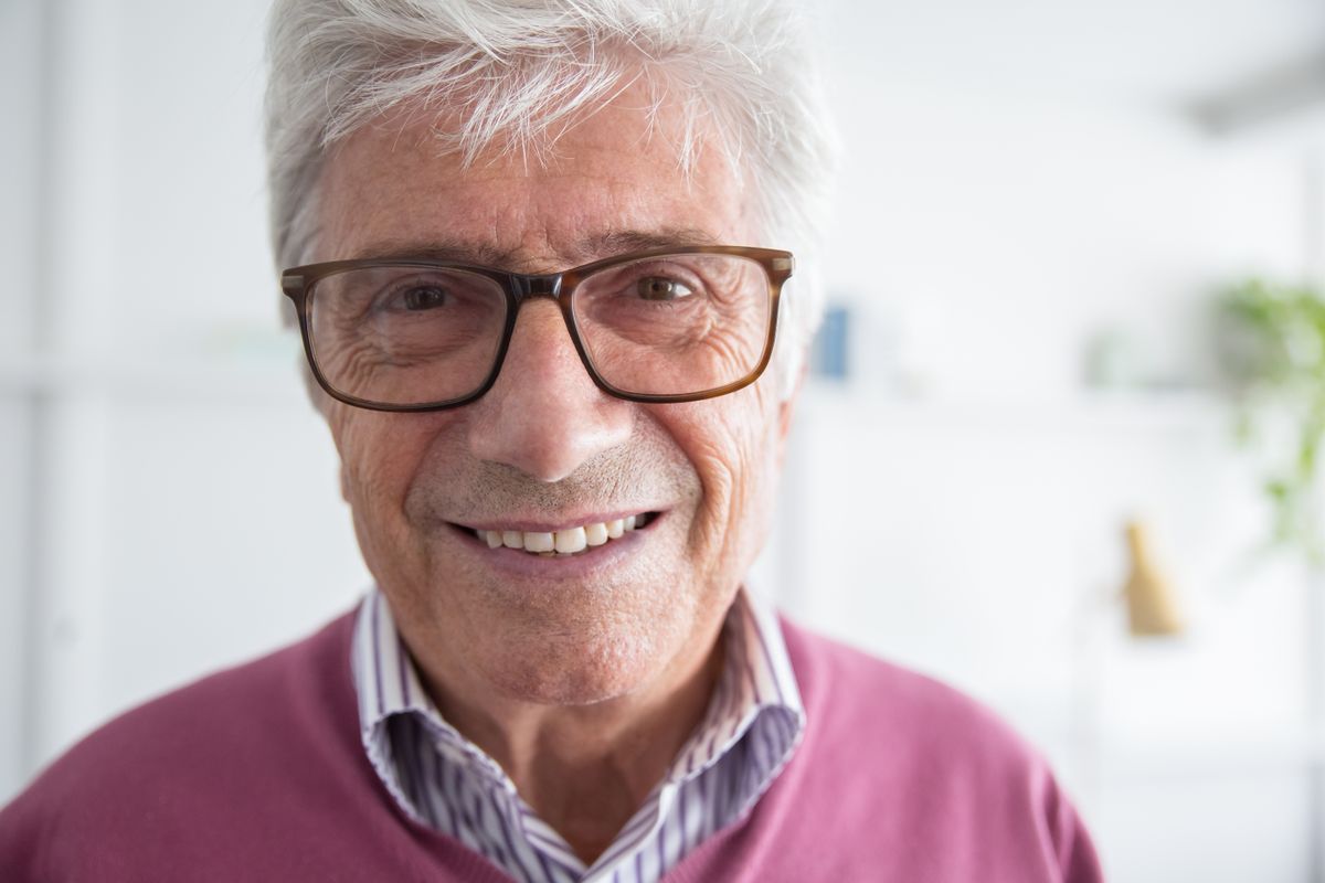 An older adult man with glasses smiling indoors.