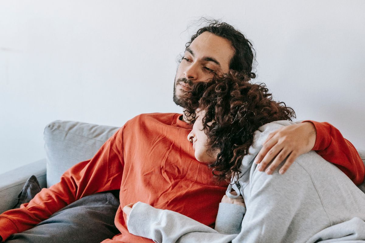 Two clothed adults leaning together while relaxing on a couch.