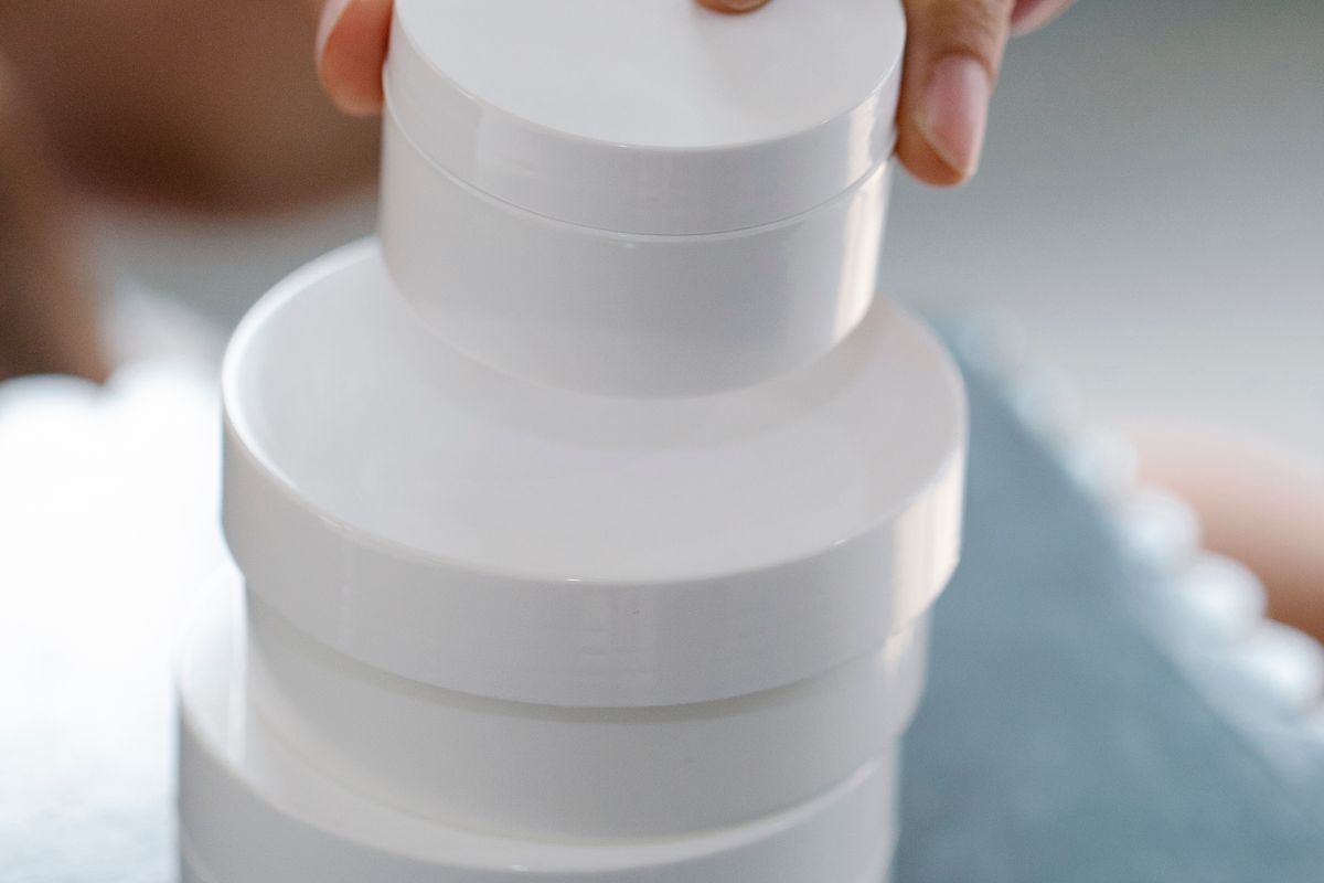 Hand arranging plain white skincare jars on a table.