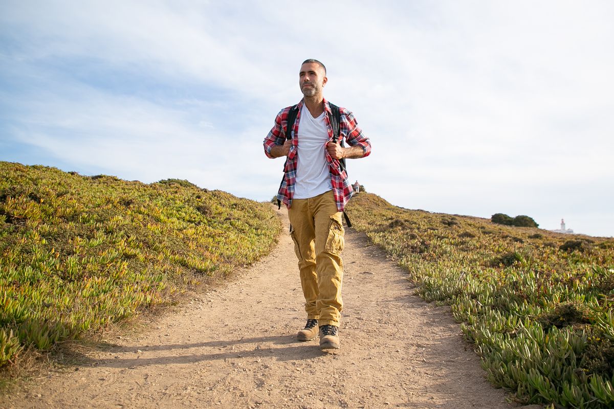 An adult man with a backpack walking on a path through low vegetation.