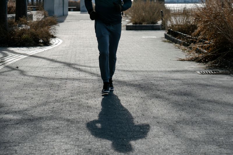 Lower-body view of an adult moving along a sunlit park path in trainers.